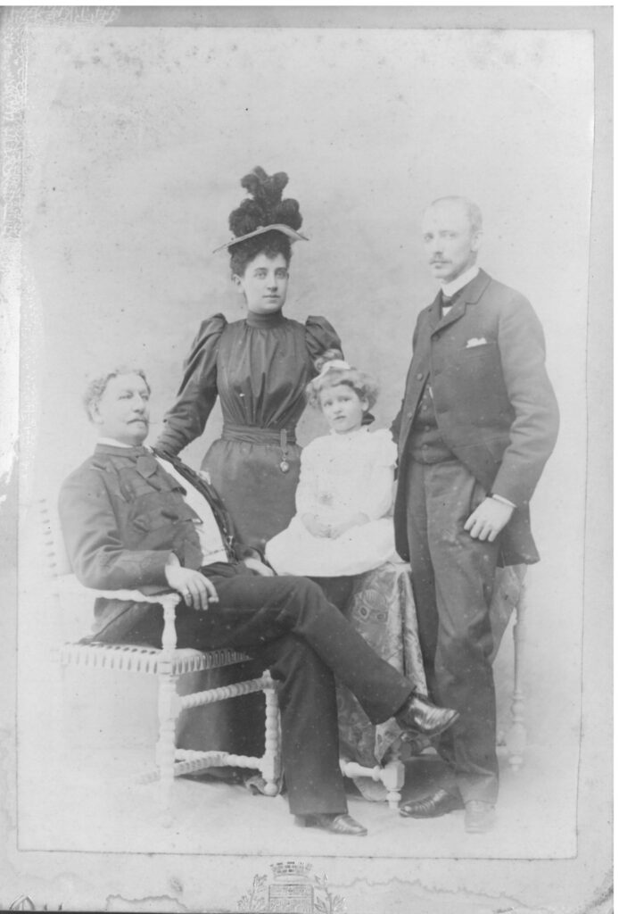 Formal family photograph.  Henry Isaac Butterfield seated in foreground, with his granddaughter seated to the left.  Stood behind them both are Jessie and Frederical