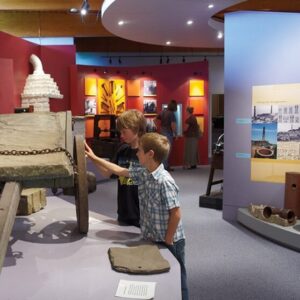 Two kids at a gallery touching an old wooden cart