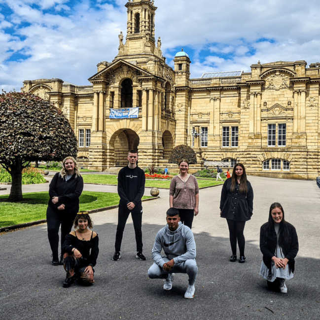7 young people posing outside of a grand building.
