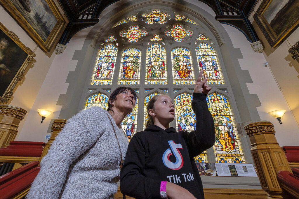 Family stood in front of Butterfield Stained Glass window, pointing