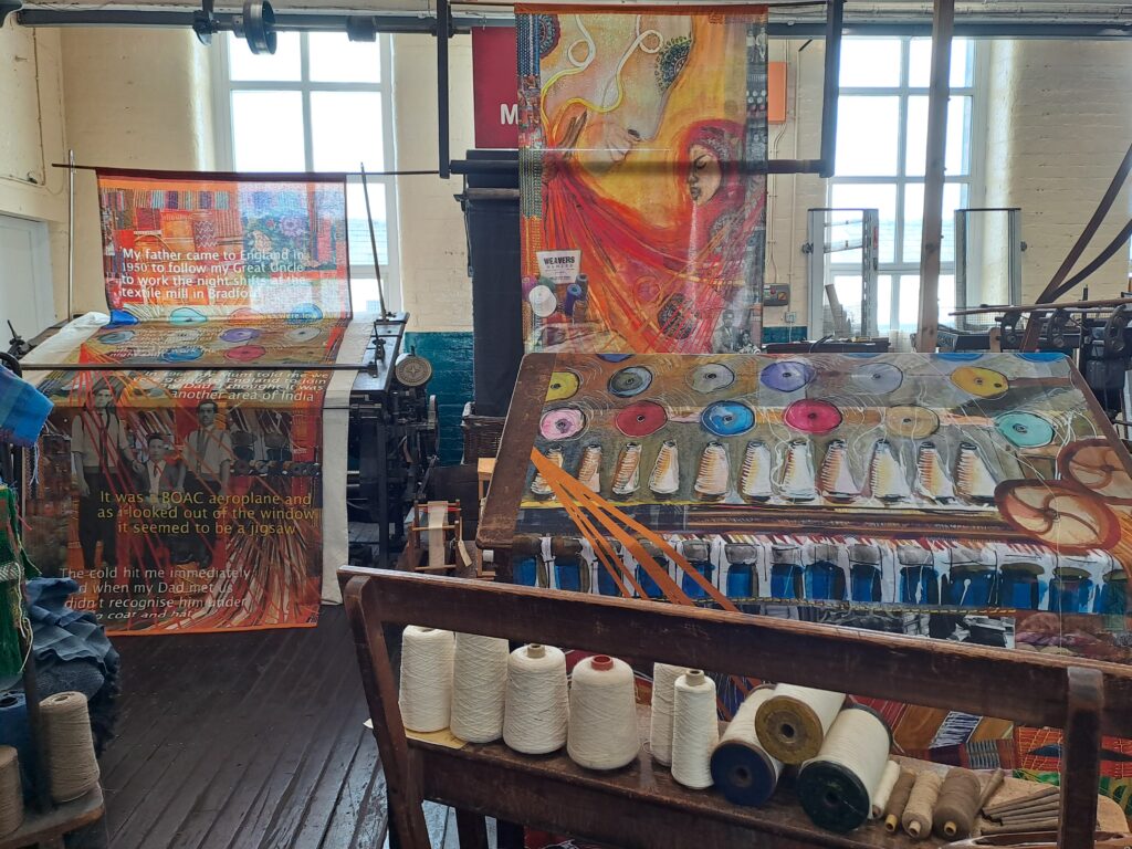Image of the gallery with the textile pieces on display, - they are very colourful depictions of parts of the machinery and process
