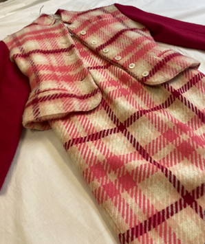 Image of a woman's suit laid on a counter. It is a plaid style pattern in light pink, dark pink and cream