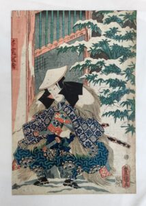 a samurai sitting outside a country house. He looks downhearted and wears a worried frown with one hand tucked up inside of his sleeve. His mino (straw overcoat) and kasa (straw hat) are covered in snow