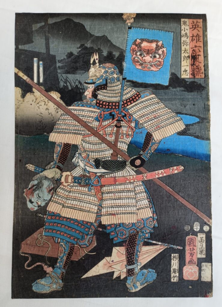 stands with the severed head of an enemy in his hand with his back to the viewer, brandishing a polearm. His kabuto (helmet) bears a crab on the front and his Sashimono (flag) features a red face demon.