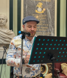 a performer standing by a microphone and music stand, mid-recitation