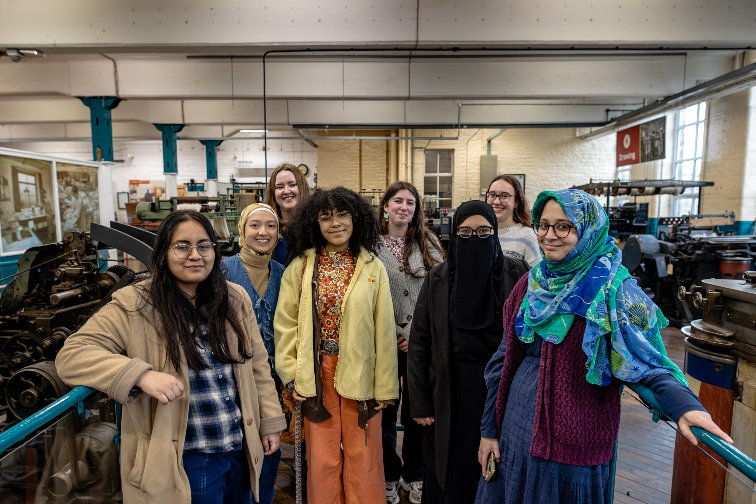 a group of young people, stood smiling in the printing gallery at Bradford Industrial Museum