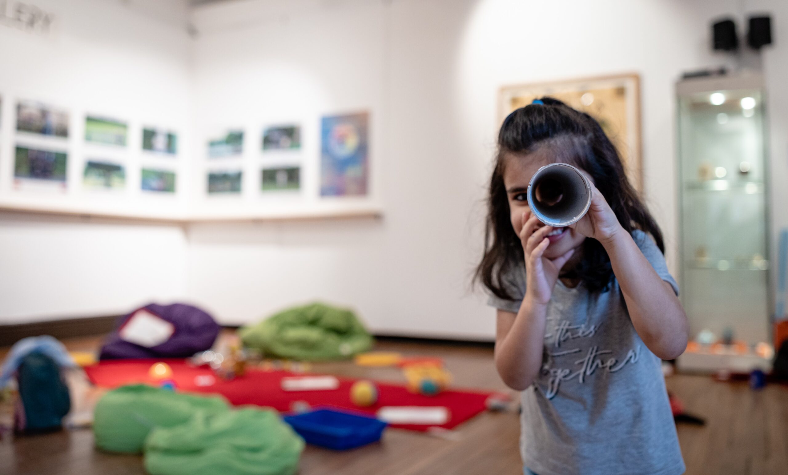 a young child in a white gallery space, looking through a tube at the viewee