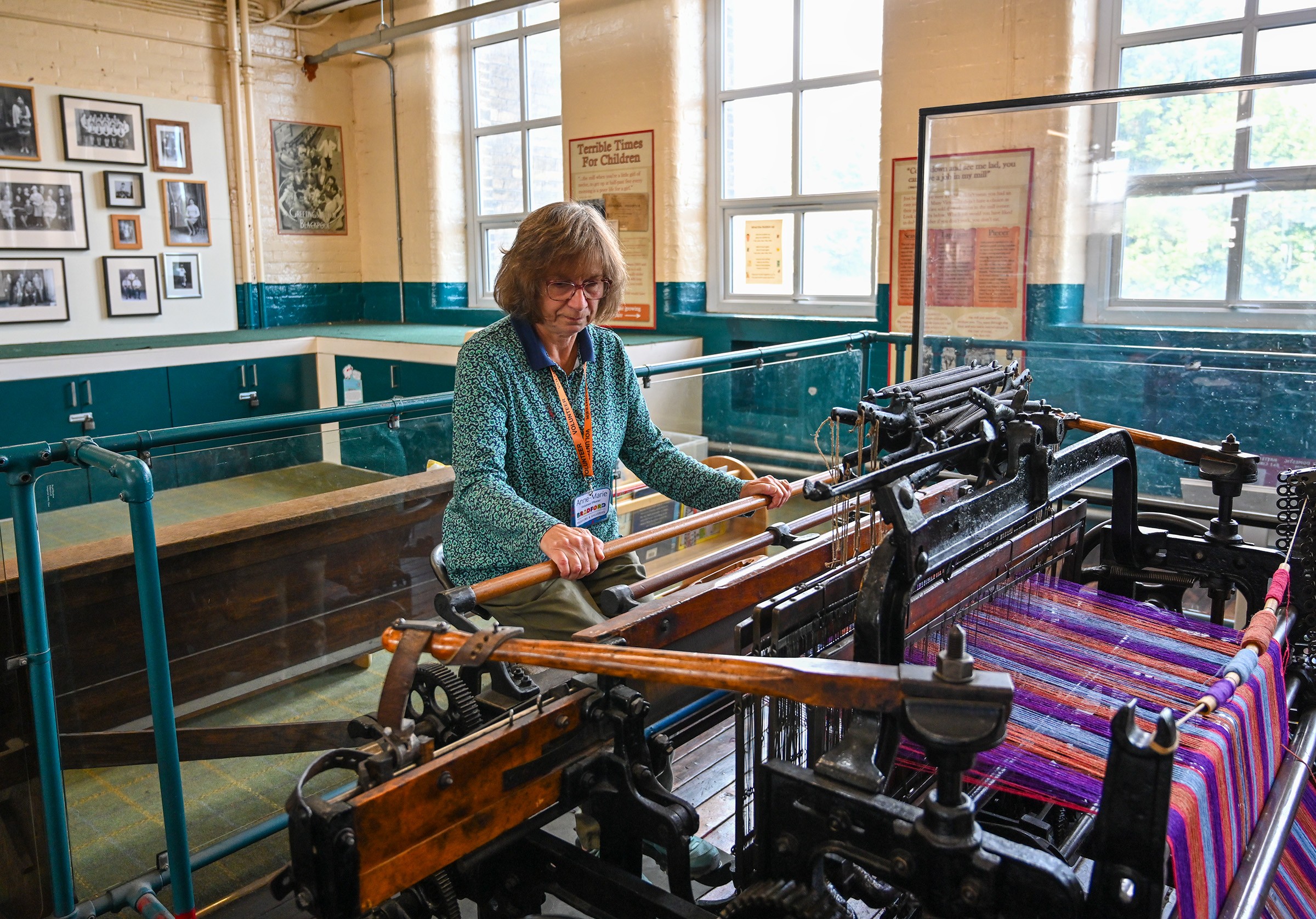 image of a person at a loom, weaving. there is a colourful textile in shades of pink and purple being woven