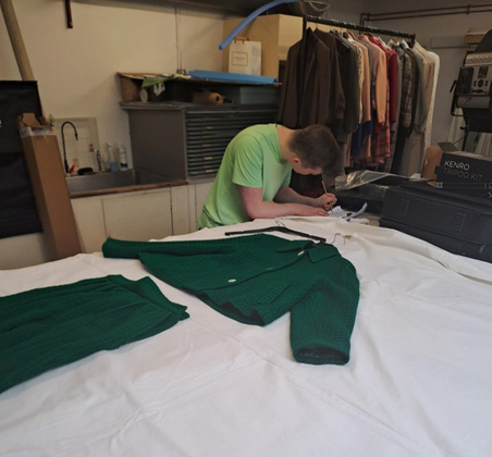 A person writing information down with a green suit laid out on the table beside them