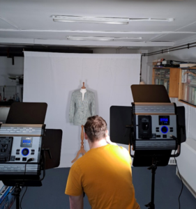 person in a yellow t-shirt taking photographs of a jacket on a mannequin