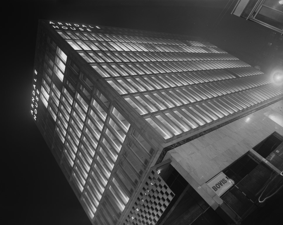 Photograph shows a completed Arndale House, Bradford. The photograph is taken at night and at an angle from the ground showing the tall building with lights on in the windows. Photographer: C H Wood, 1965. In Bradford District Museums and Galleries collection (71534).