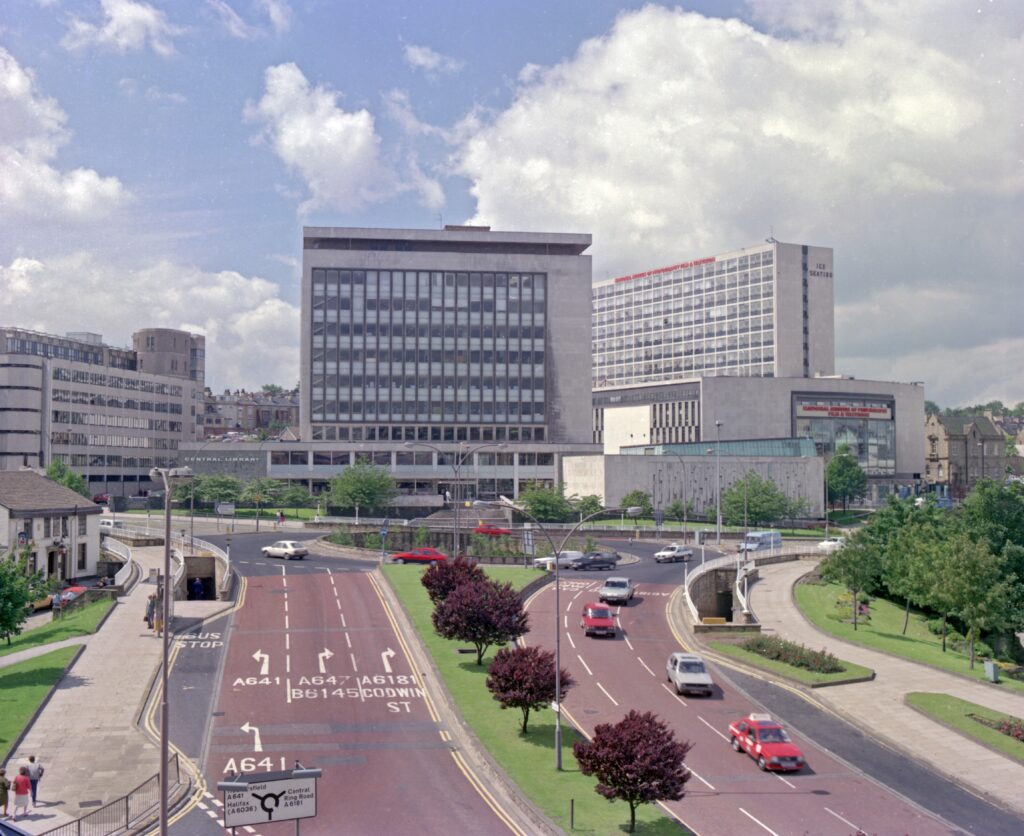 Photographs shows Hall Ings, Bradford, with the ring road and Jacob’s Well roundabout. In the background, there is the National Museum of Photography, Film and Television (now the National Science and Media Museum), the old Central Library building and the ice rink. Photographer: C H Wood, 1987. In Bradford District Museums and Galleries collection (162140).