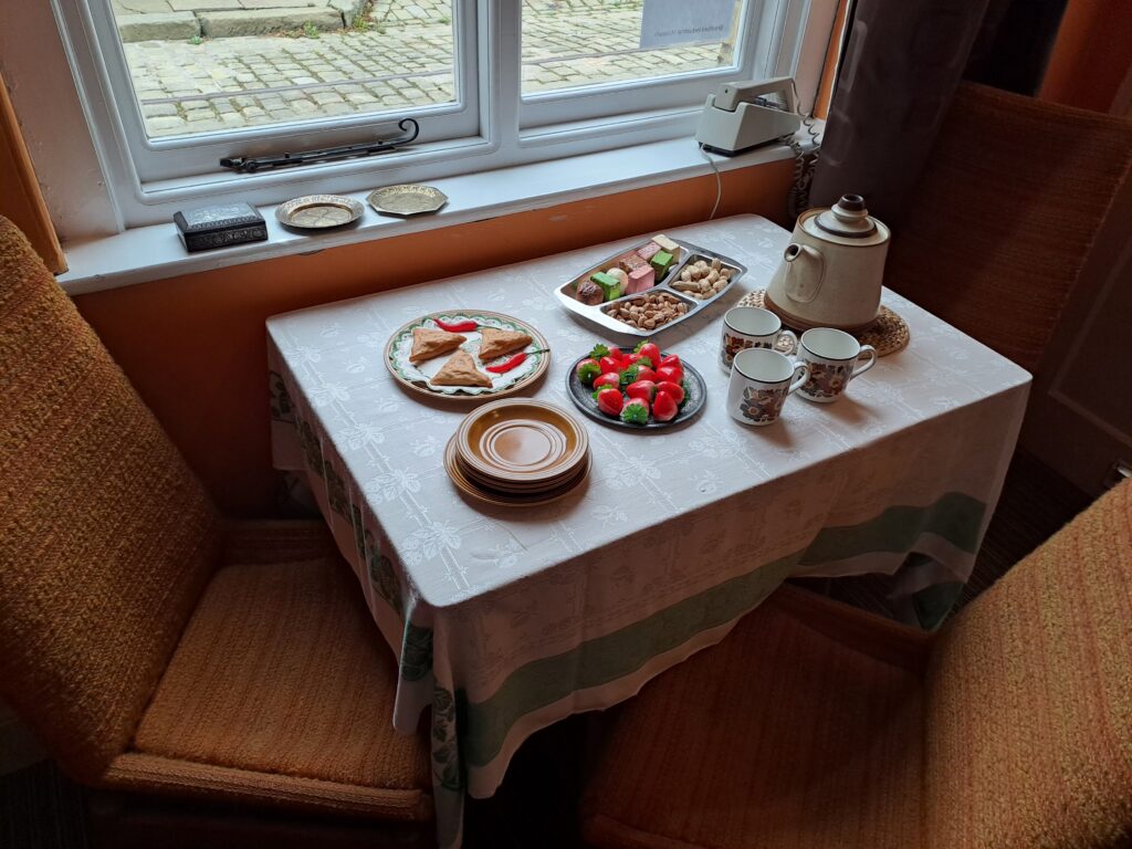 food out on a table-  samosas, pakastani sweets, strawberries, alongside a teapot and teacups