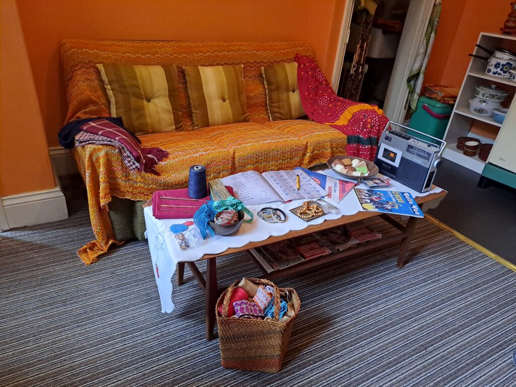 sofa and coffee table visible, mending on view, as well as a cassette radio ont he table, and colourful throws