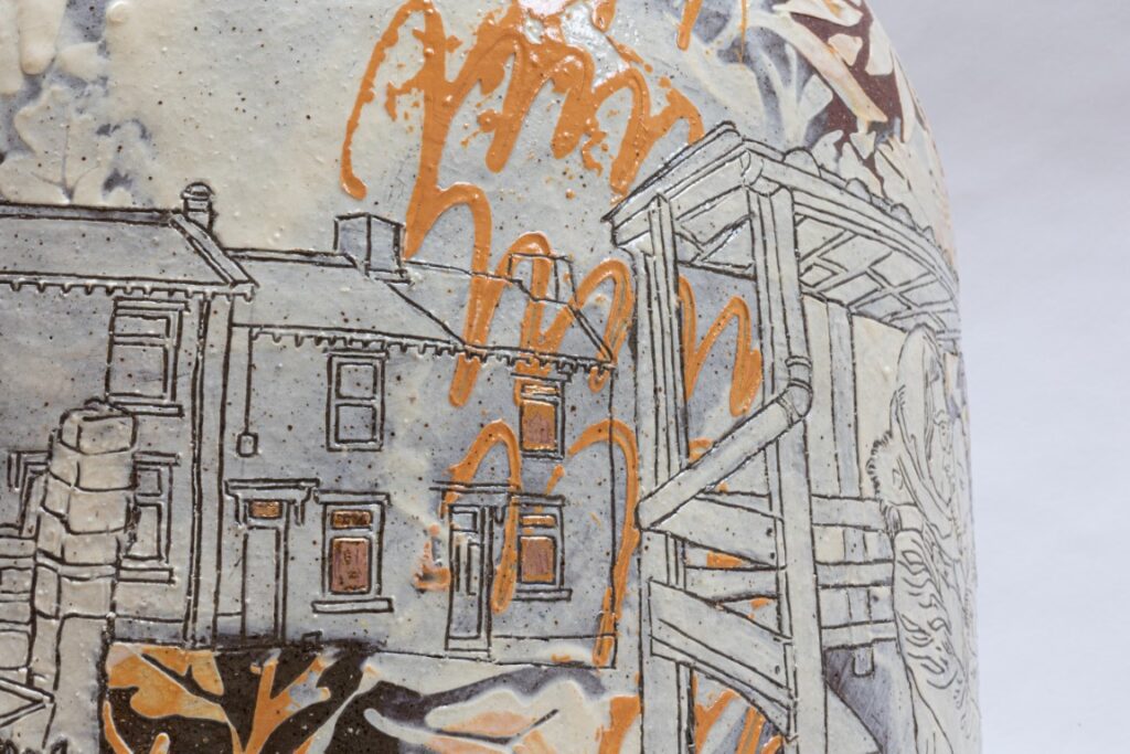 Close up of details on the vase.  Depicted are terraced houses and and a shelter for the gardeners.  Most of the background is white slip, with the lines of the image removed to show the underlying brown ceramic