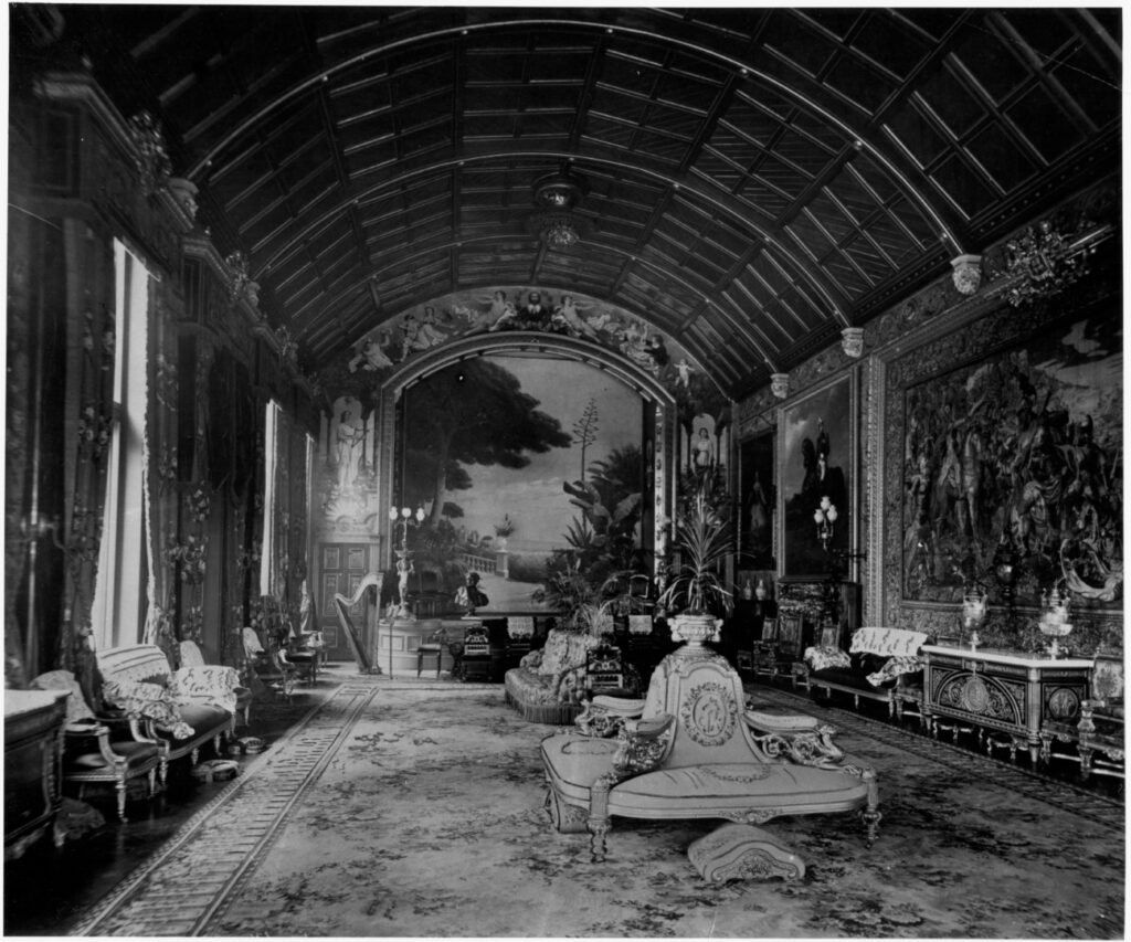 B&W photo of the ballroom at Cliffe Castle. Visible is a large stage with painted backdrop, various music instruments visible 