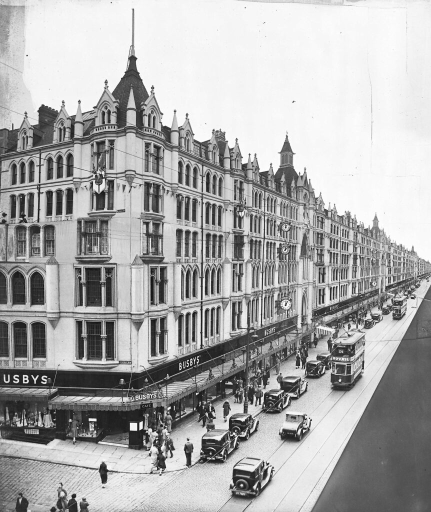 Black and white photo of Busbys Department store in Bradford. 1950s cars are visible on the road in front