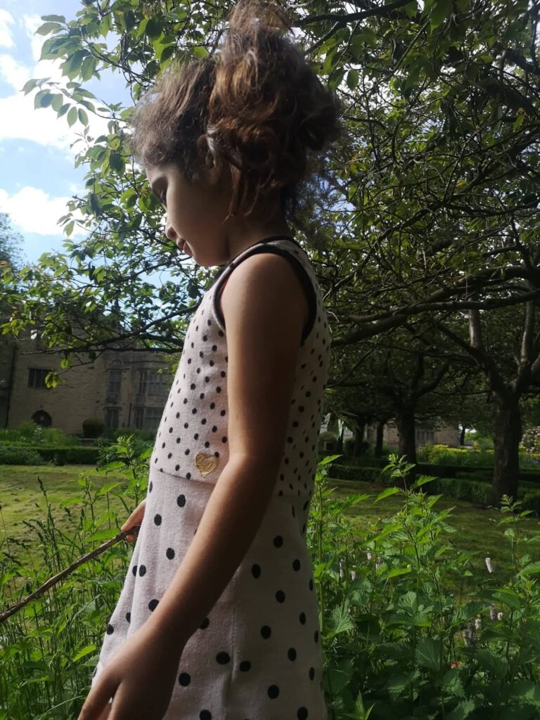 Young girl looking down at the grass, side on to the photographer, with Bolling Hall in the background of the image