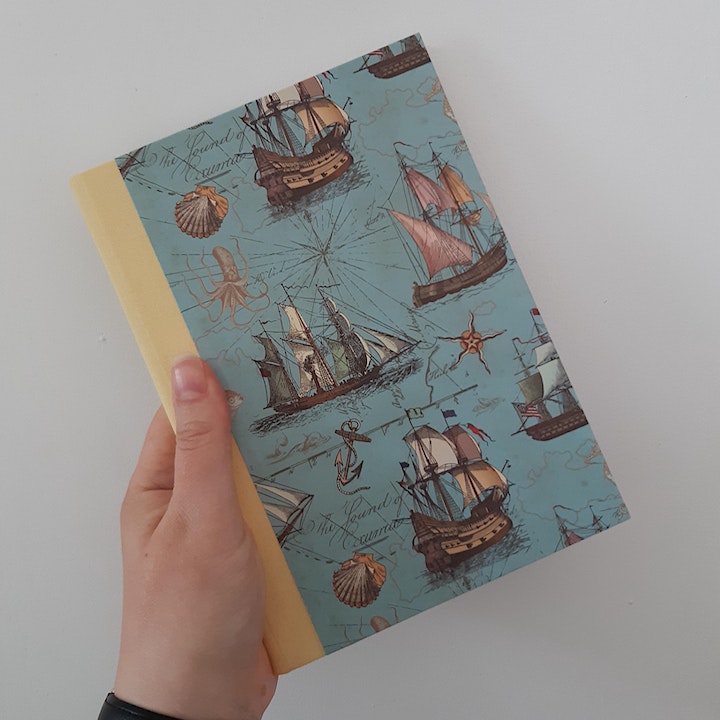 a hand holding a book, bound with a design of ships