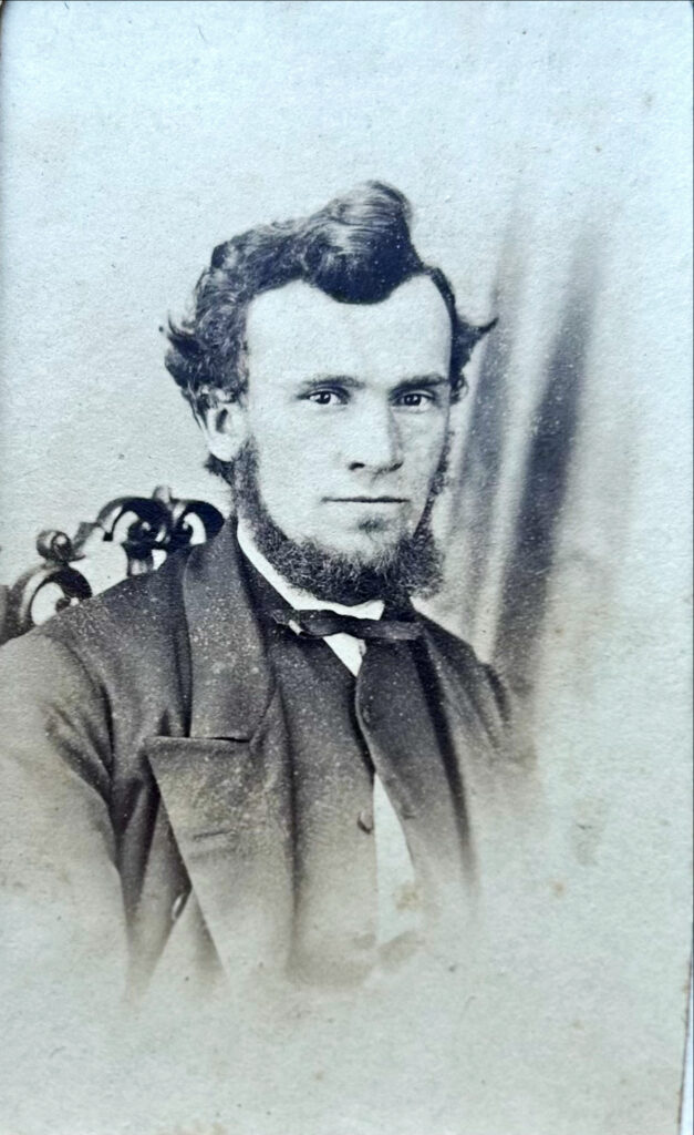 B&W head and shoulders photograph of a white man, dark suit, He has bouffant dark hair, and a beard, but no mustache. He is looking at the camera