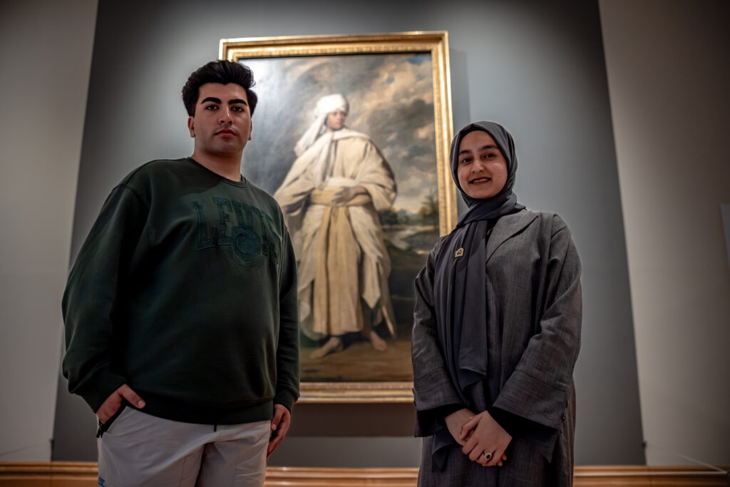 image of two young people in front of the portrait.  