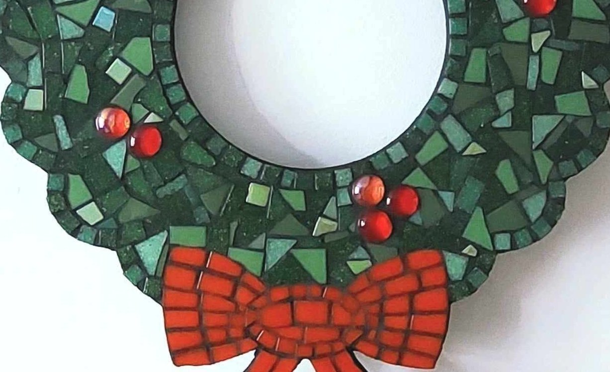 Close up of mosaic christmas wreath. Mostly in shades of green, with some red 'berries' and a red bow - all made of mosaic