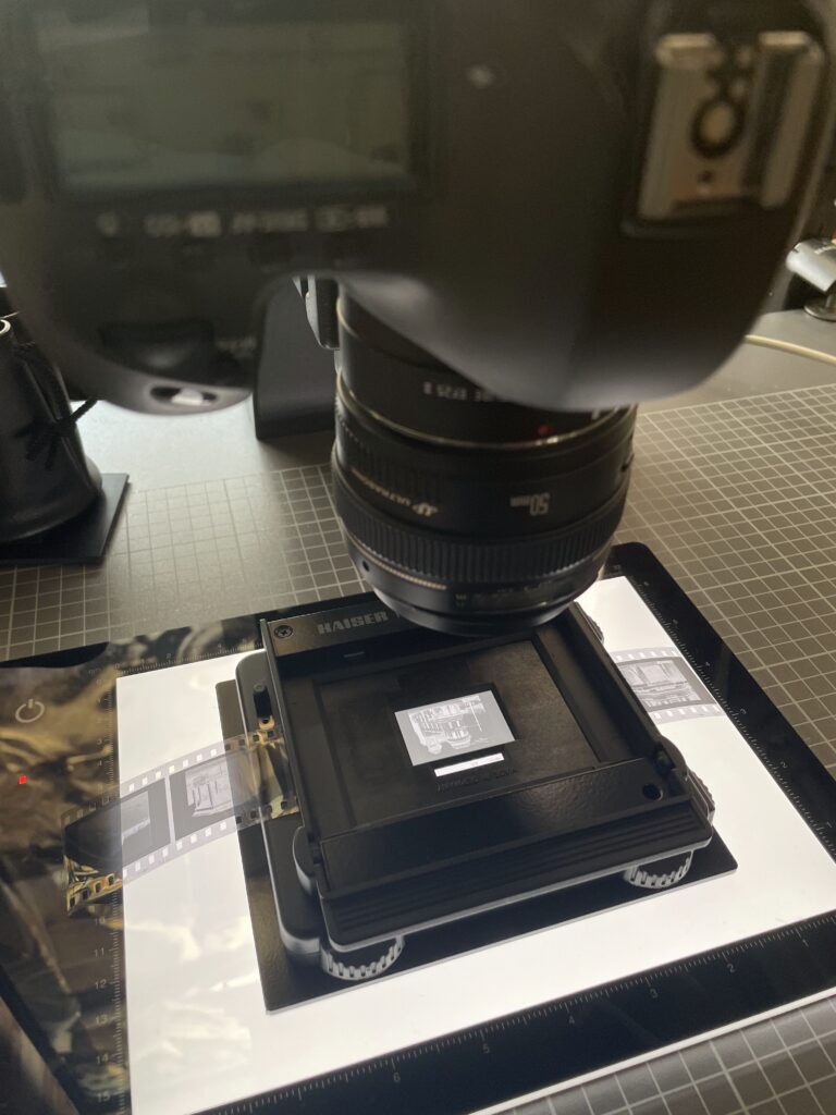 a strip of black and white negatives on a digitisation set up - a light box behind the negative and a camera above it.