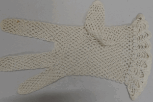 A cream-colored crochet gloves laid flat on a light surface. The glove features an open lace-like pattern with scalloped edges at the wrist, giving it a delicate and decorative appearance. There are 3 fingers and a thumb