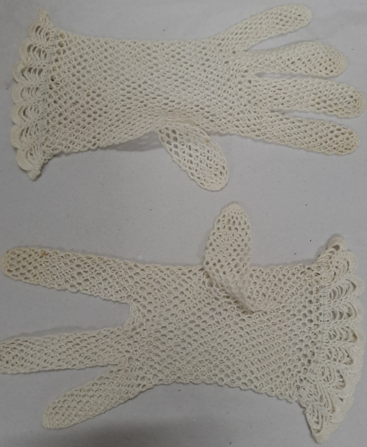 A pair of vintage, cream-colored crochet gloves laid flat on a light surface. The gloves feature an open lace-like pattern with scalloped edges at the wrist, giving them a delicate and decorative appearance. Both gloves are positioned with the fingers extended, showing their intricate handmade design.
The bottom glove in the image has only 3 fingers.