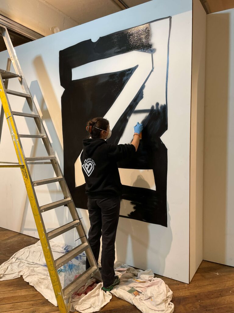 a person spray painting a large 'Z' on a gallery wall