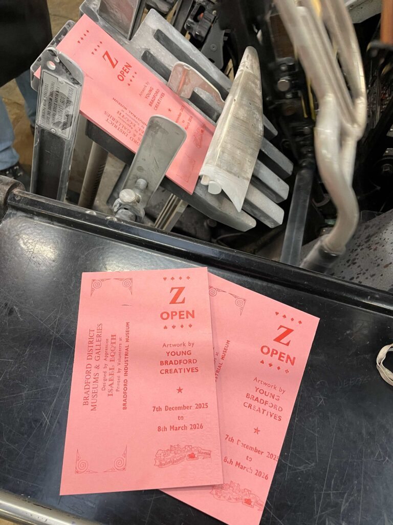 pink bookmark stating 'Z Open, Artwork by Young Bradford Creatives, 7th December - 8th March, Bradford Industrial Museum, designed by Apprentice Isabel Booth, printed by print volunteers at Bradford Industrial Museum'