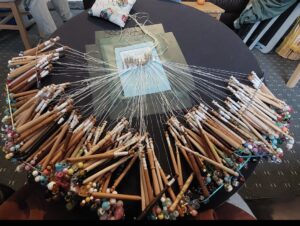 photograph of a piece of bobbin lace in progress, resting on the pillow, with the bobbins in view
