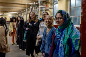 A group of people standing in an industrial heritage space with exposed pipes and machinery,