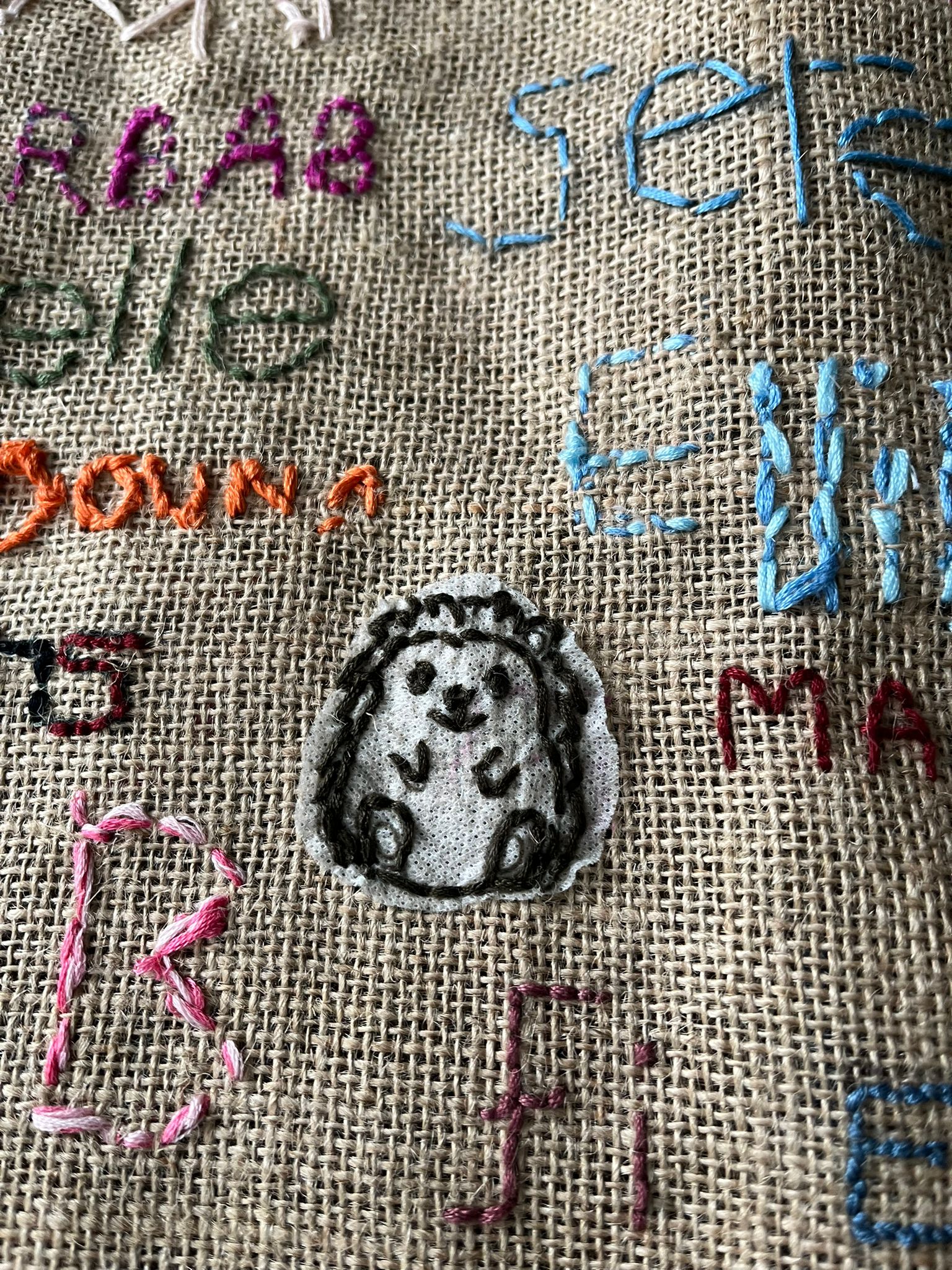 close up of a section of brown jute fabric, with multi coloured embroidery on it