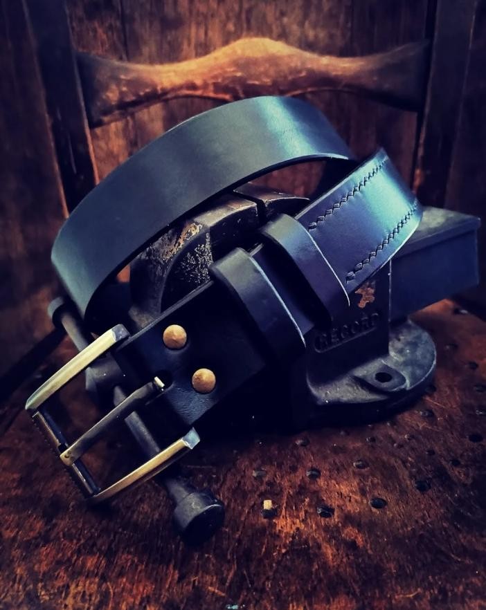 black leather belt, coiled on a wooden backdrop