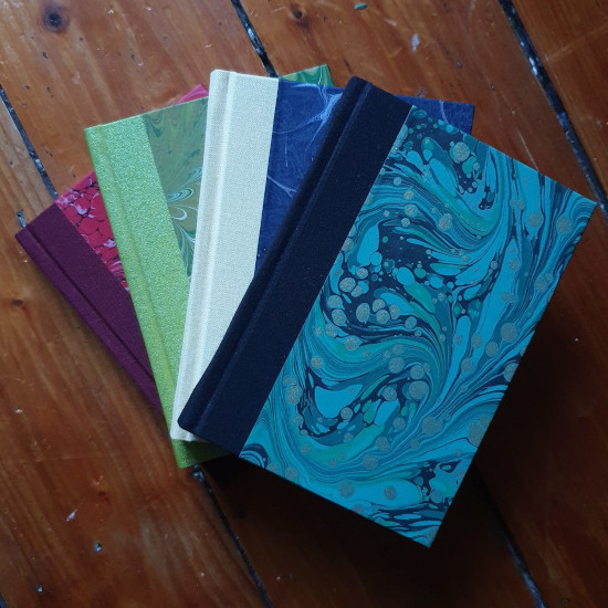 a photo of a group of traditionally bound note books with marbeled covers in a range of colours