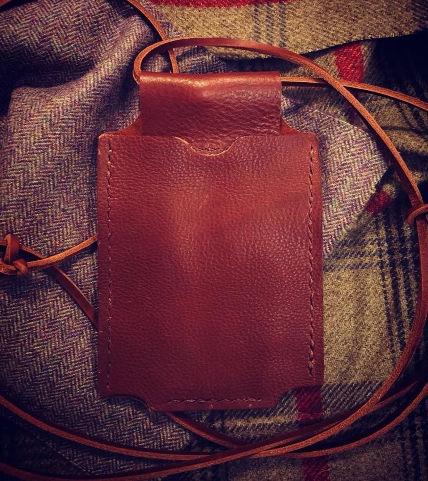 warm brown leather phone holder on a background of tweed material (in shades of brown and yellow)