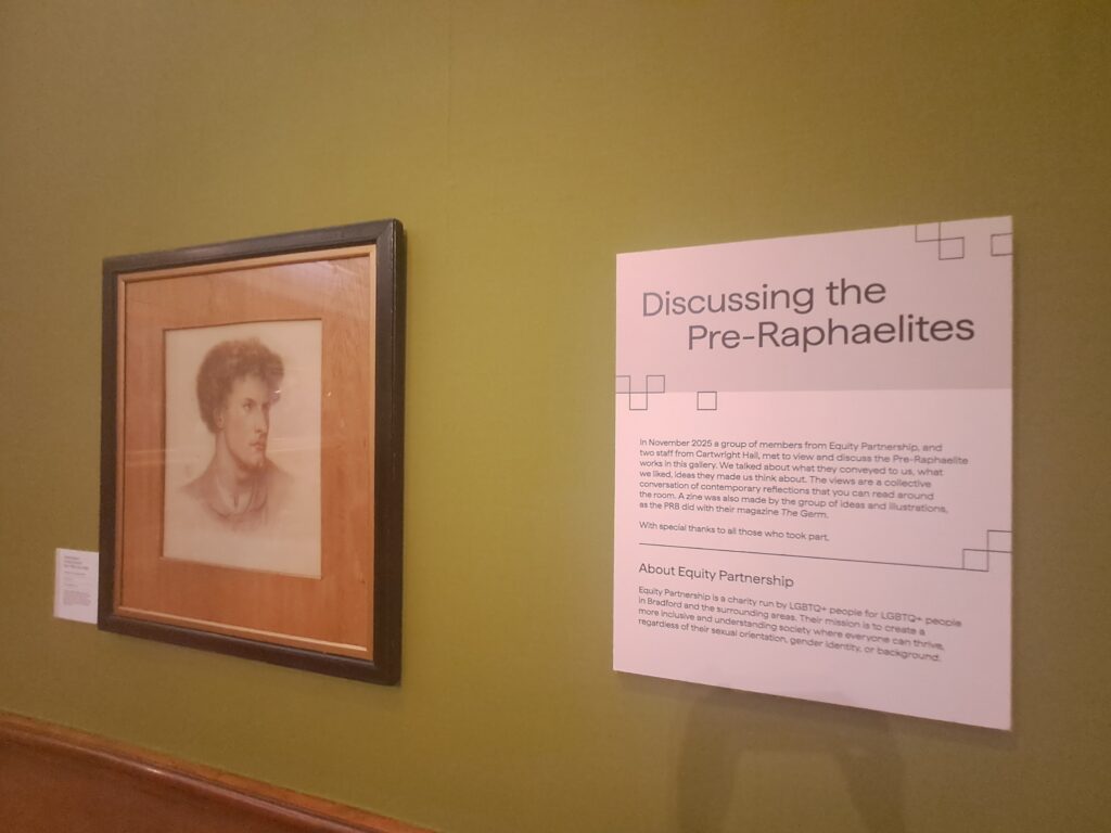 A framed pencil portrait of a person with short curly hair hangs on a green gallery wall beside an information panel titled “Discussing the Pre-Raphaelites.” The panel explains a 2025 discussion event between Equity Partnership members and Cartwright Hall staff, and includes a short description of the LGBTQ+ charity