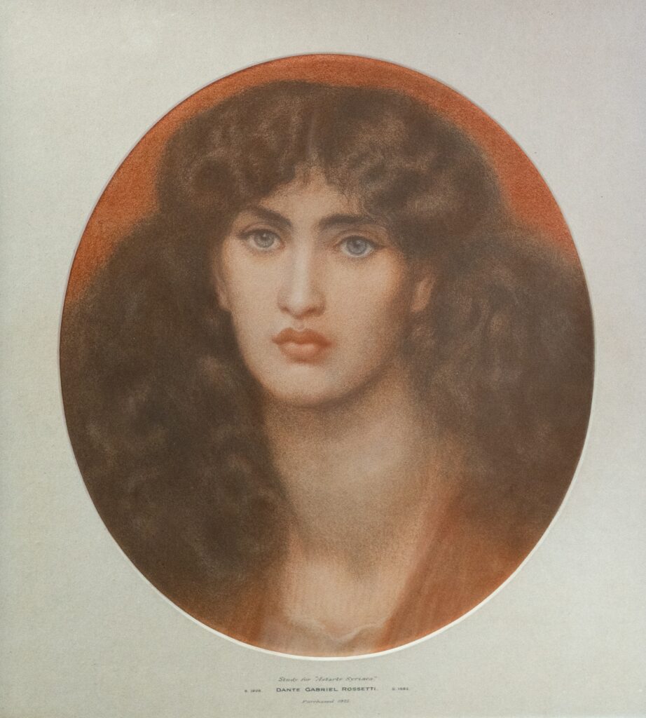 An oval portrait study of a person with long dark hair and blue eyes, shown against a warm reddish‑brown ground. The sitter faces forward with a steady gaze. Printed text beneath identifies the work as a study for “Astarte Syriaca” by Dante Gabriel Rossetti