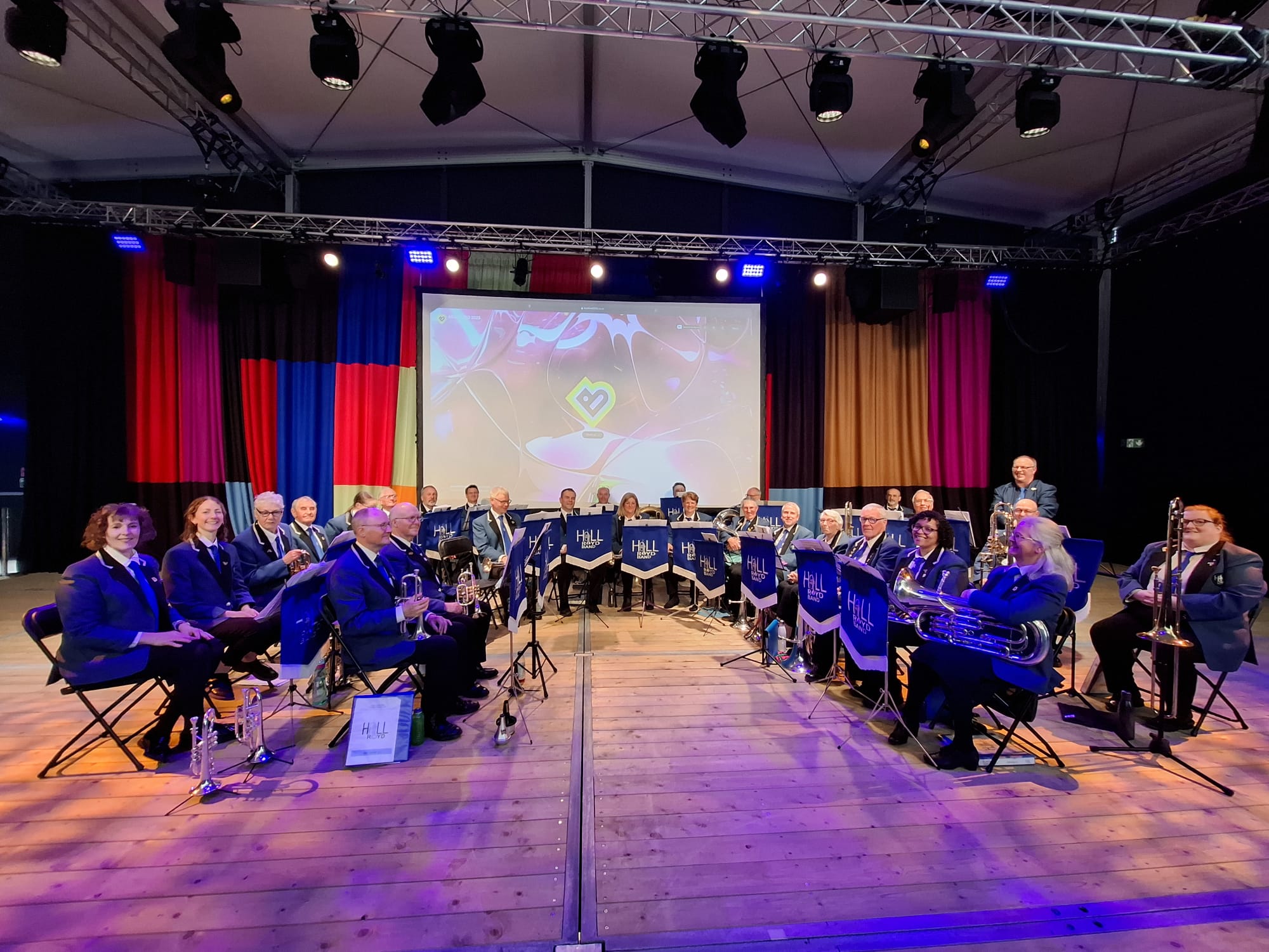 A seated brass band in matching blue uniforms on a stage.